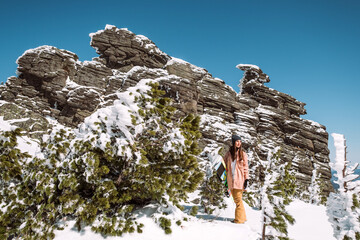 Wall Mural - Russia. Sheregesh. Girl snowboarder in winter in sunny weather outdoors among the Christmas tree, huge rock and snow. The girl is standing with a snowboard in her hands and posing. 