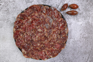 Wall Mural - Portion of acorn-fed Iberian sausage 100% acorn on black plate decorated with acorns and gray background