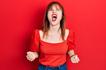 Wall Mural - Redhead young woman wearing casual red t shirt angry and mad screaming frustrated and furious, shouting with anger. rage and aggressive concept.