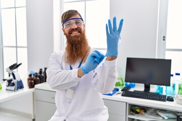 Canvas Print - Young redhead man wearing scientist uniform wearing gloves at laboratory