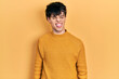 Handsome hipster young man wearing casual yellow sweater sticking tongue out happy with funny expression. emotion concept.