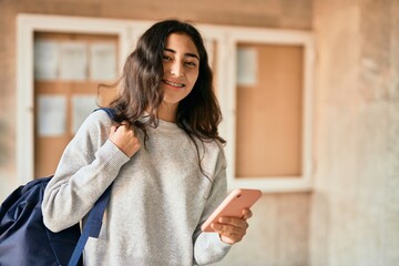 Wall Mural - Young middle east student girl smiling happy using smartphone at the city.