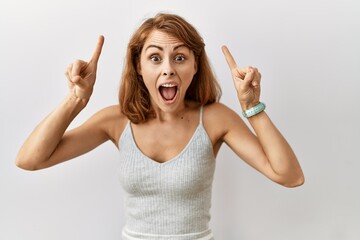 Sticker - Beautiful caucasian woman standing over isolated background smiling amazed and surprised and pointing up with fingers and raised arms.