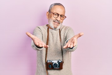 Poster - Handsome senior man with beard holding vintage camera looking at the camera smiling with open arms for hug. cheerful expression embracing happiness.