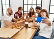 © Krakenimages.com - Group of young friends smiling happy eating italian pizza making selfie by the smartphone at home.