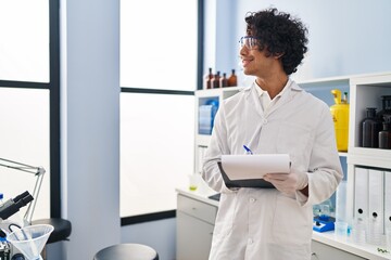 Sticker - Young hispanic man wearing scientist uniform writing on clipboard at laboratory