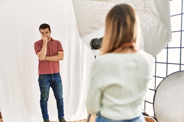 Wall Mural - Woman photographer talking pictures of man posing as model at photography studio looking stressed and nervous with hands on mouth biting nails. anxiety problem.