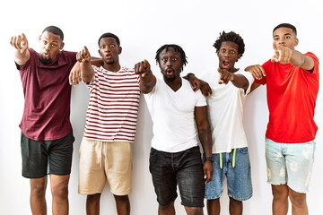 Canvas Print - Young african group of friends standing together over isolated background pointing with finger surprised ahead, open mouth amazed expression, something on the front