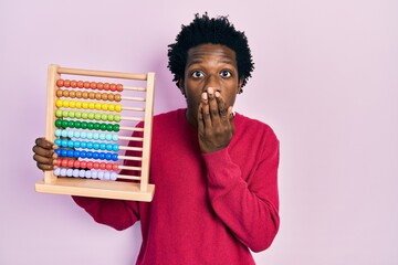 Sticker - Young african american man holding traditional abacus covering mouth with hand, shocked and afraid for mistake. surprised expression