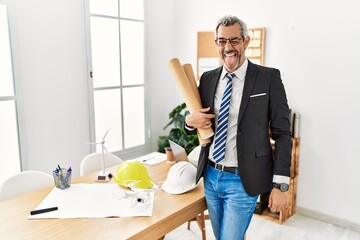 Canvas Print - Middle age hispanic business man holding paper blueprints sticking tongue out happy with funny expression. emotion concept.