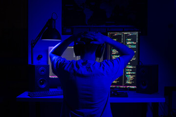 a disappointed man sits at a computer in a room at a table at night with blue lighting and programs