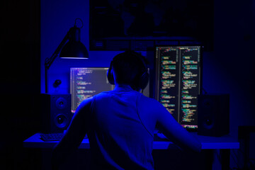a man sits at a computer in a room at a table at night with blue lighting and programs