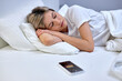 Alarm clock on smartphone lying on bed near sleepy caucasian woman to wake up on early morning, at home. female in pajamas. Early awakening, not getting enough sleep, oversleep concept