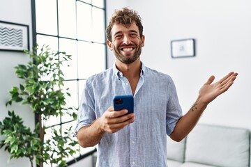 Wall Mural - Young handsome man using smartphone at home celebrating achievement with happy smile and winner expression with raised hand