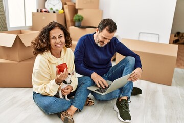 Poster - Middle age hispanic couple using laptop and drinking coffee. Sitting on the floor with dog at new home.