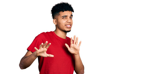 Young african american man wearing casual red t shirt disgusted expression, displeased and fearful doing disgust face because aversion reaction. with hands raised