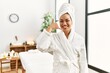© Krakenimages.com - Young brunette woman wearing towel and bathrobe standing at beauty center smiling doing phone gesture with hand and fingers like talking on the telephone. communicating concepts.