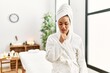© Krakenimages.com - Young brunette woman wearing towel and bathrobe standing at beauty center feeling unwell and coughing as symptom for cold or bronchitis. health care concept.