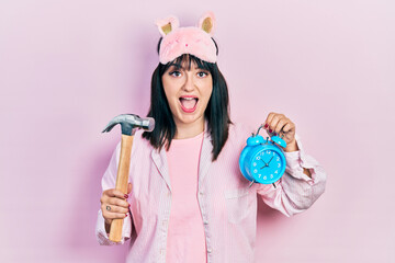 Sticker - Young hispanic woman wearing sleep mask and robe holding alarm clock and hammer celebrating crazy and amazed for success with open eyes screaming excited.