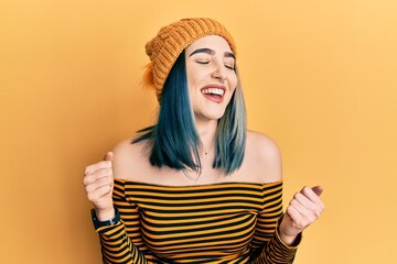 Wall Mural - Young modern girl wearing wool hat very happy and excited doing winner gesture with arms raised, smiling and screaming for success. celebration concept.