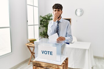 Sticker - Hispanic man with beard voting putting envelop in ballot box bored yawning tired covering mouth with hand. restless and sleepiness.