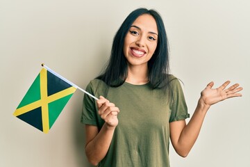 Wall Mural - Young hispanic girl holding jamaica flag celebrating achievement with happy smile and winner expression with raised hand