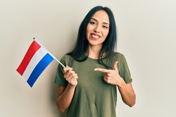 Wall Mural - Young hispanic girl holding holland flag smiling happy pointing with hand and finger