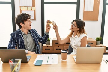 Wall Mural - Two business workers smiling happy toasting with doughnuts at the office.