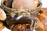 Fototapeta Panele - Assorted bread and sweet buns in a basket with spikelets of wheat on a white background