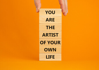 You artist of your life symbol. Wooden blocks with words You are the artist of your own life. Beautiful orange background, copy space. Businessman hand. Business, motivational lifestyle concept.