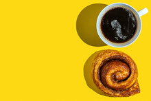 Cup Of Coffee And Sticky Bun On Yellow Background With Copy Space.