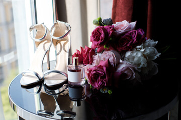 Beautiful wedding bouquet of roses and greenery, huge shoes and perfume on the table