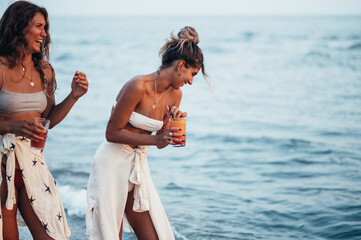 Attractive friends enjoying vacation together on the beach and drinking cocktails