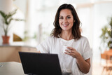 Fototapeta Pomosty - happy smiling remote working woman drinking coffee or espresso infront of a laptop or notebook on her work desk in her modern airy bright living room home office 