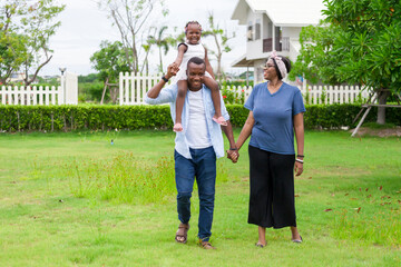 Wall Mural - .Happy family of African American people with young little daughter walking on green grass field while enjoying summer garden outside the house in the neighborhood