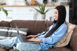 © kucherav - Lifestyle, young smiling Asian woman lying down on sofa using laptop to browse social networks, shopping. Having a good time at home