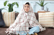 © kucherav - Ill Asian young woman sitting on the couch at home covered with blanket feeling unwell, has a cold or flu