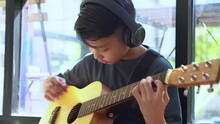 Asian Boy Learning To Play The Guitar In Virtual Meeting For Play Music Online Together With Friend Or Teacher In Video Conference With Laptop For Online, Communication Over Internet Learning Concept