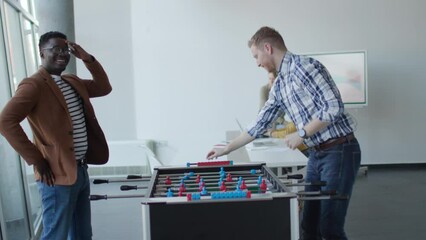 Wall Mural - Young handsome casual multiethnic business people playing table football and relaxing at office