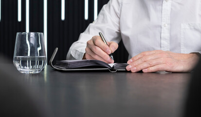 Poster - Closeup hands taking notes in planner, planning business appointments. Businessman sitting at desk and writing in notebook. Agenda concept.