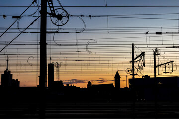 Silhouettes at sunset of electrical train equipment, wires, cables, lines and poles, Leuven, Belgium