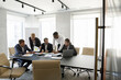 © fizkes - Multiethnic team of businesspeople analyzing startup project sales reports on meeting in boardroom. Corporate teacher, mentor training group of interns with paper charts