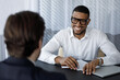 © fizkes - Happy African intern meeting with mentor, company coach, listening to teacher, smiling, laugh. Job seeker meeting business owner for interview. Manager, banker giving consultation to client