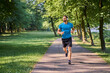 © baranq - Young man jogging in a park on a sunny summer day listens to music on headphones