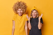 Happy upbeat young female companions laugh out loudly at funny joke feel euphoric express positive emotions dressed casually isolated over vivid yellow background. People and happiness concept
