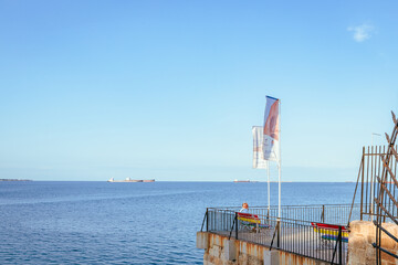 Wall Mural - Man sitting on bench by the sea with tankers in the background