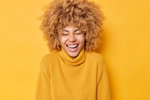 Photo Of Overjoyed European Woman Laughs Sinecerely Smiles Broadly Has Upbeat Mood Keeps Eyes Closed Wears Casual Warm Jumper Isolated Over Yellow Background. Authentic Happy Emotions Concept
