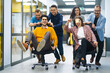 © maxbelchenko - Young cheerful business people  having fun while racing on office chairs and smiling. Friendly work team enjoying fun work break activities.