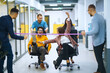 © maxbelchenko - Young cheerful business people  having fun while racing on office chairs and smiling. Friendly work team enjoying fun work break activities.