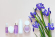 Delicate floral cosmetics for facial skin care, hands and make-up and bouquet of spring flowers of blue irises on light background. Spring rejuvenation concept. Copy space, flat lay, top view, closeup